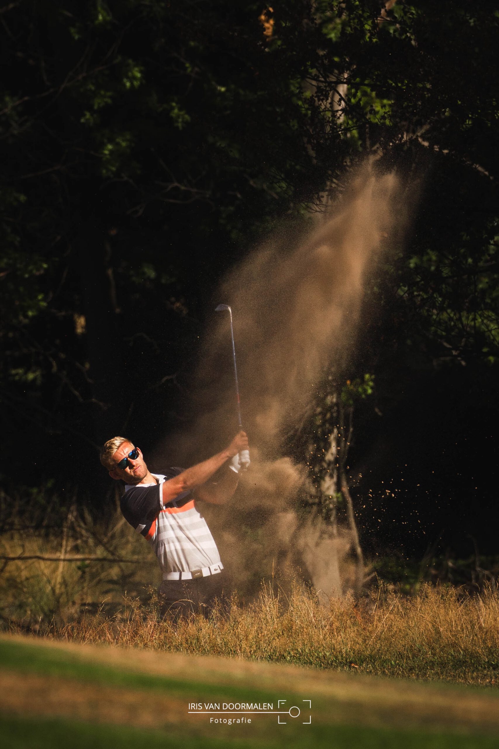 golfer slaat bal uit de bunker, zand in de lucht