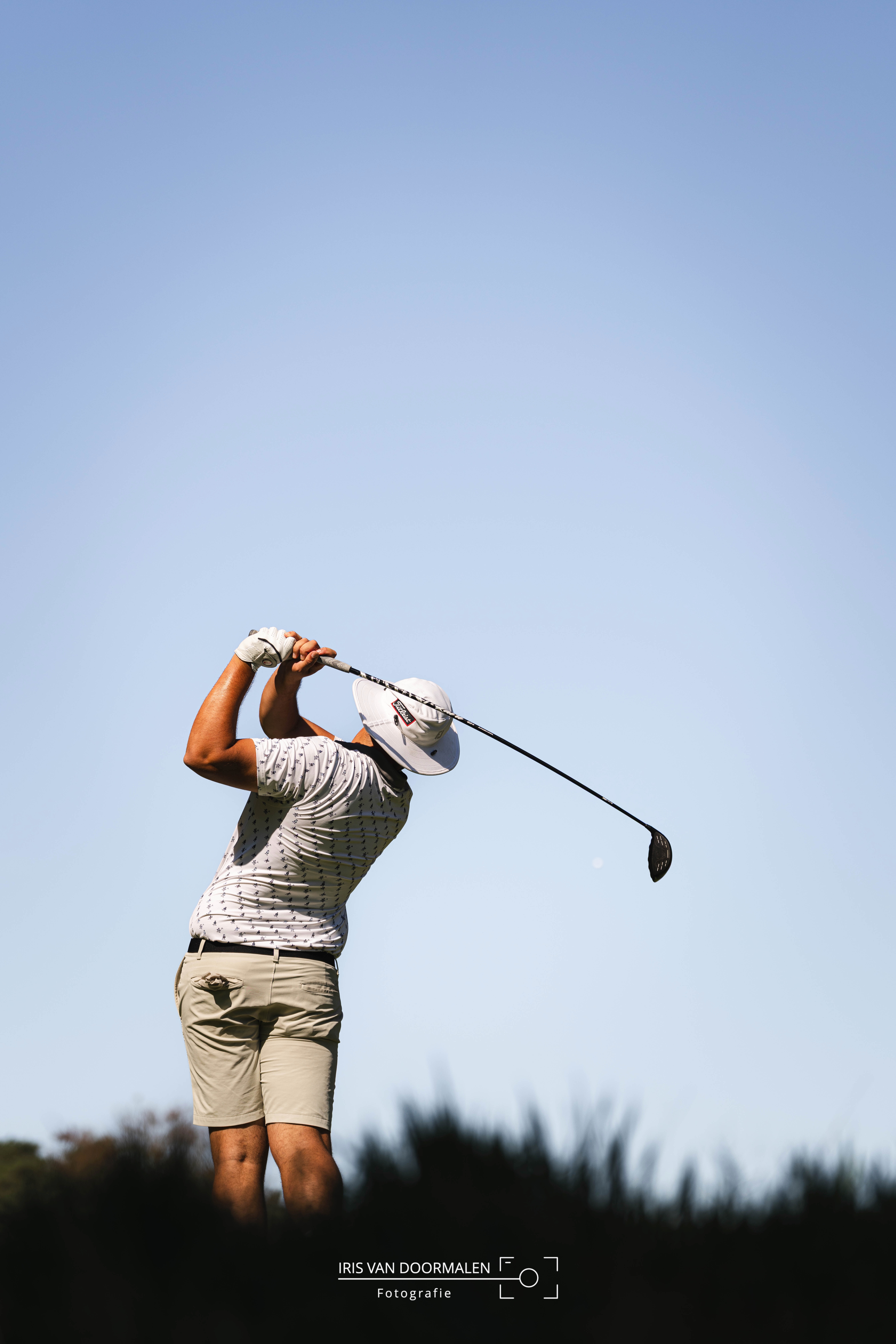 golfer met hoedje heeft bal weggeslagen, strakblauwe lucht