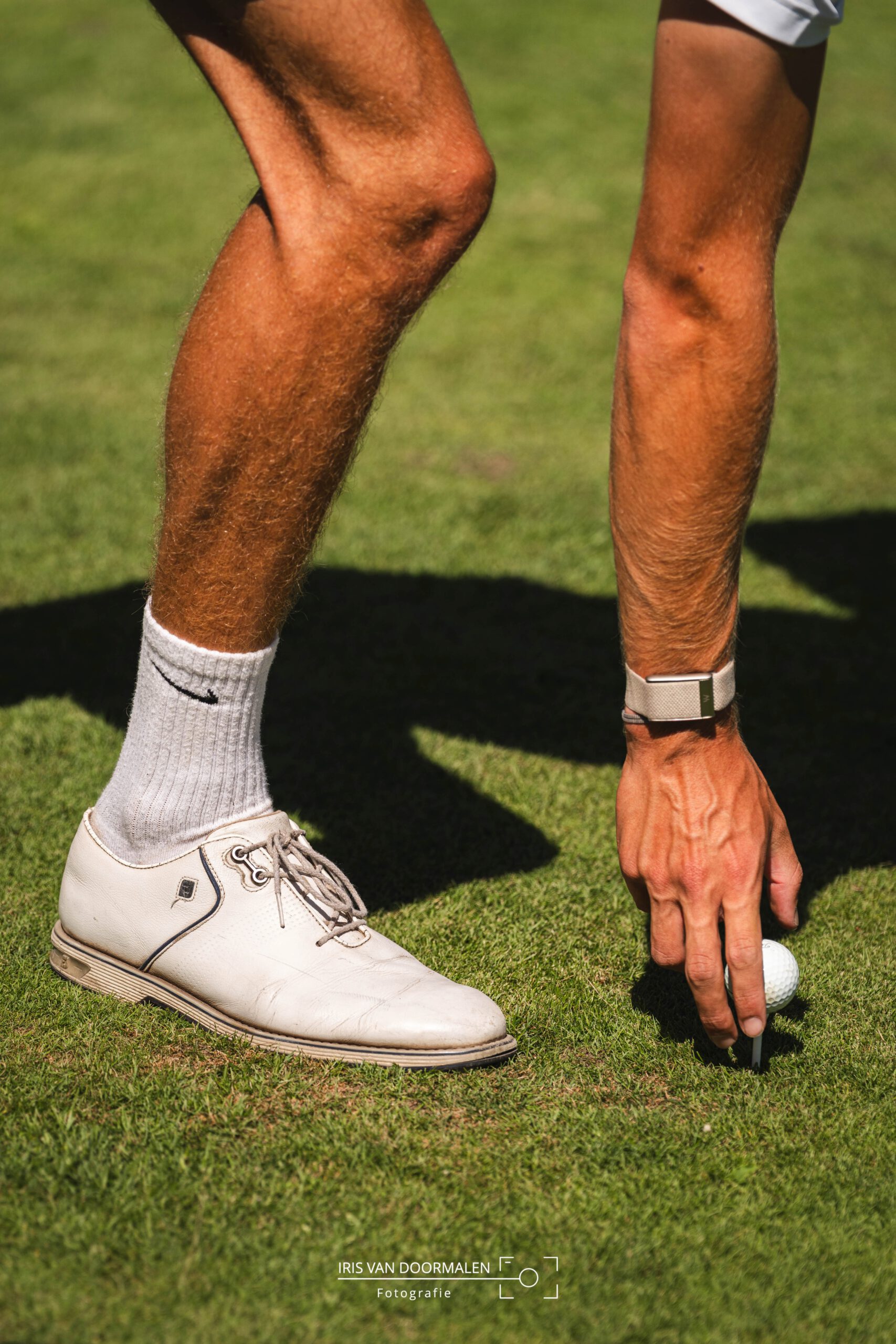 golfer legt bal op tee, gespierde been en arm zichtbaar op foto