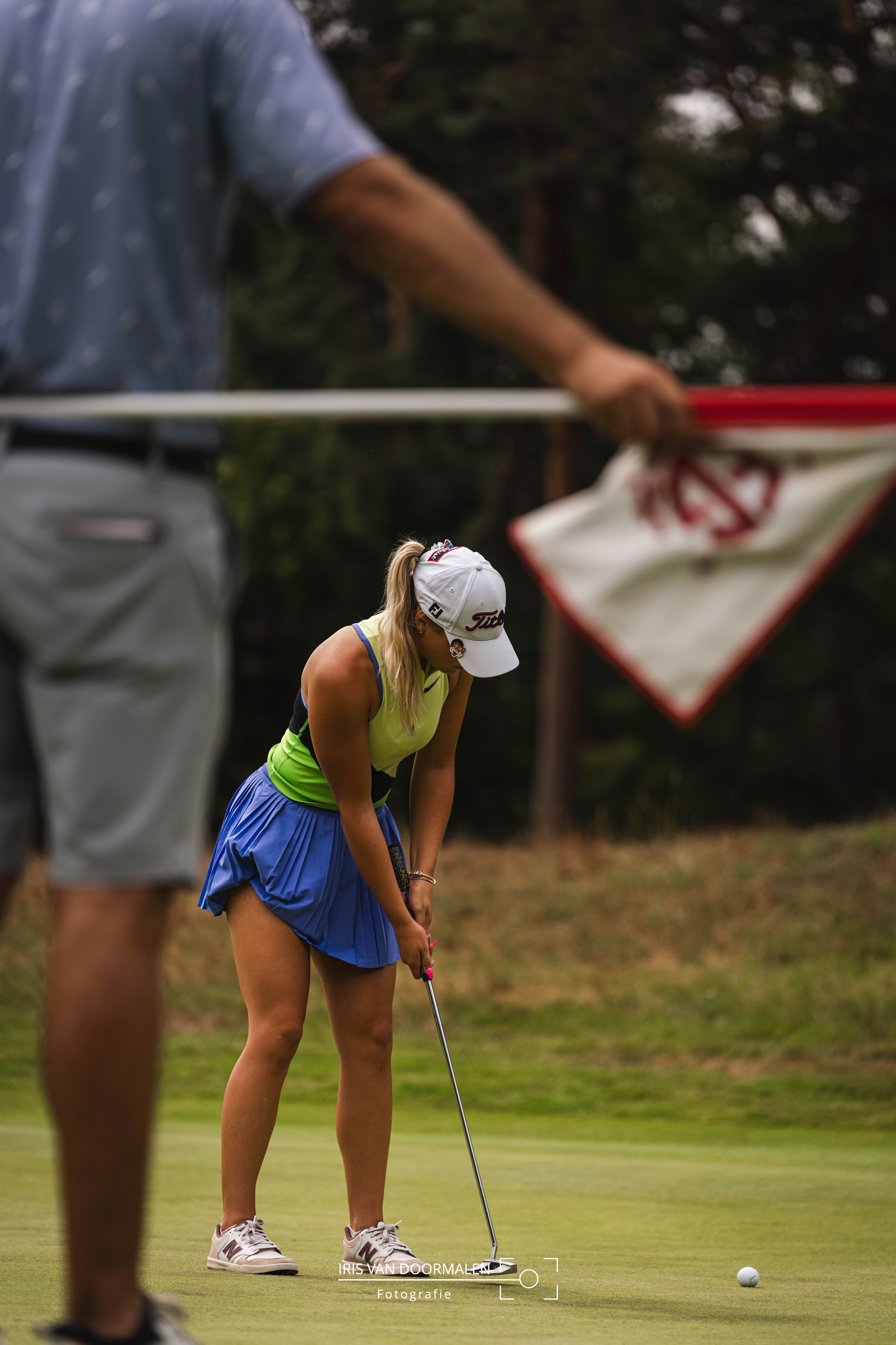 golfer is aan 't putten, op voorgrond houdt caddy de vlag vast