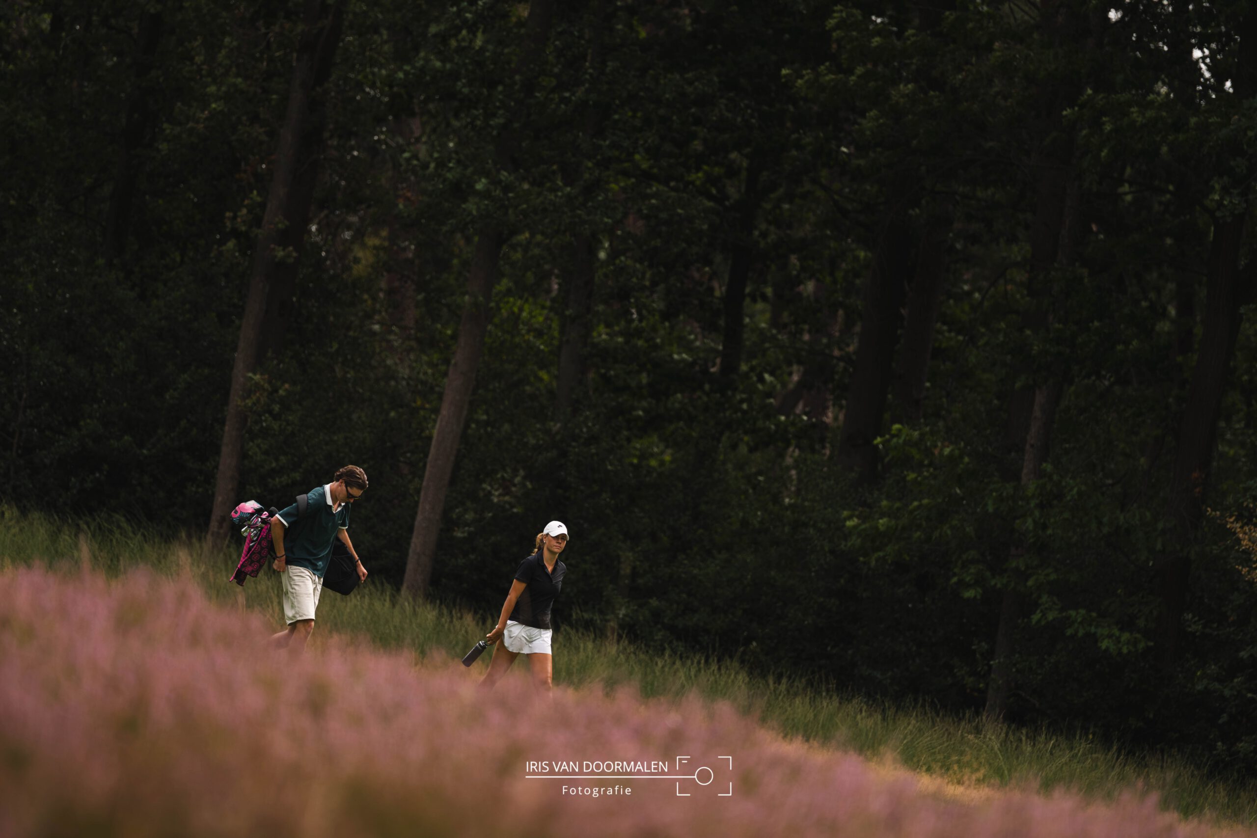 golfer en caddy lopen over de fairway, heide op voorgrond